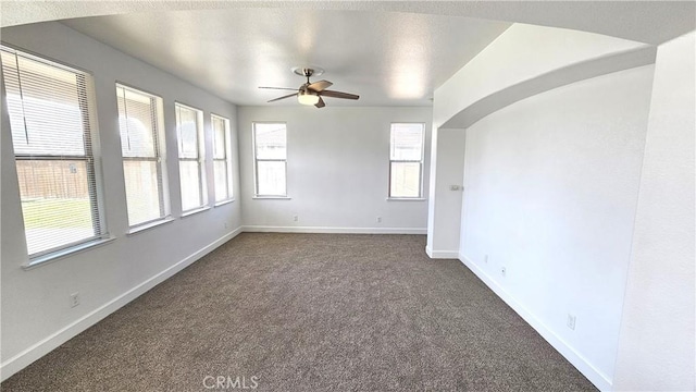 spare room featuring arched walkways, ceiling fan, baseboards, and dark colored carpet