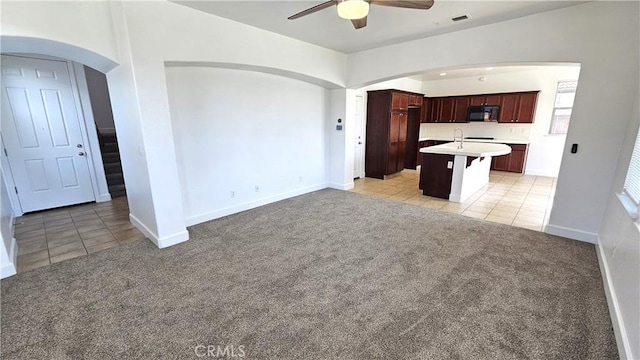 unfurnished living room featuring arched walkways, light colored carpet, and light tile patterned flooring