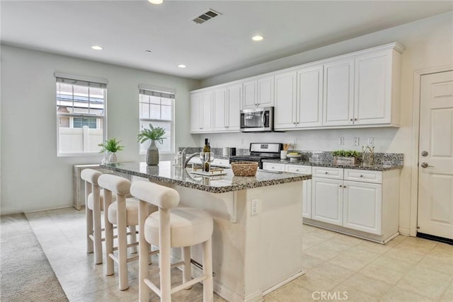 kitchen featuring visible vents, a breakfast bar, dark stone countertops, appliances with stainless steel finishes, and white cabinets