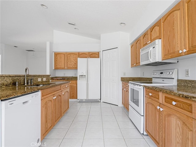 kitchen featuring white appliances, dark stone countertops, light tile patterned flooring, and a sink