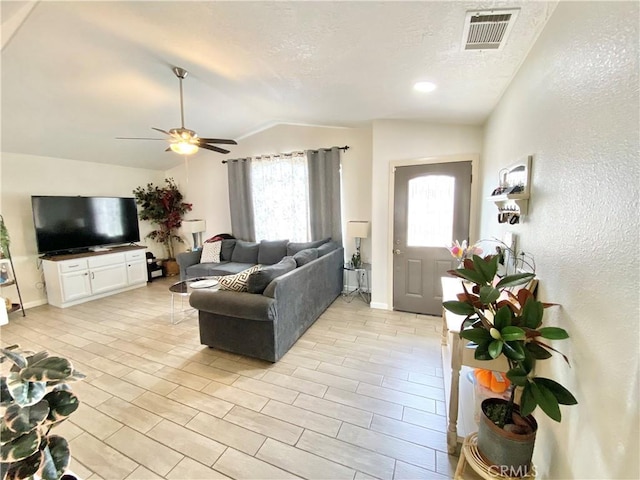 living room with visible vents, vaulted ceiling, a textured wall, a textured ceiling, and a ceiling fan