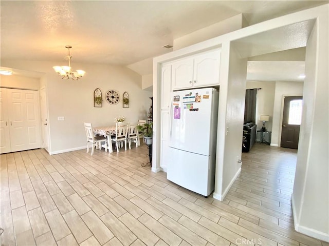 kitchen with light wood finished floors, lofted ceiling, freestanding refrigerator, white cabinets, and a chandelier