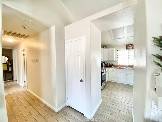 kitchen with stainless steel gas range oven, visible vents, wood finish floors, a sink, and white cabinets