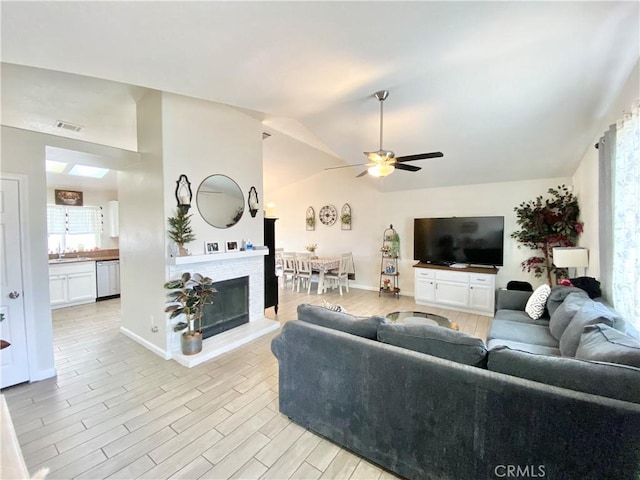 living room with ceiling fan, baseboards, vaulted ceiling, a fireplace, and light wood-style floors