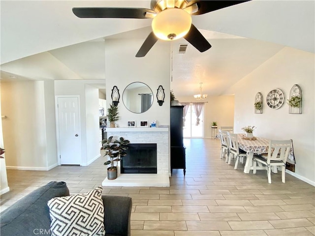 living area featuring wood finish floors, a fireplace with raised hearth, ceiling fan with notable chandelier, baseboards, and vaulted ceiling