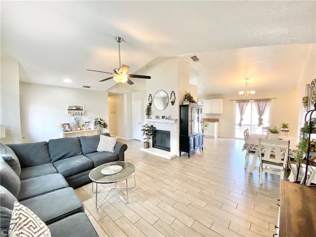 living area featuring visible vents, light wood-style floors, a glass covered fireplace, and vaulted ceiling