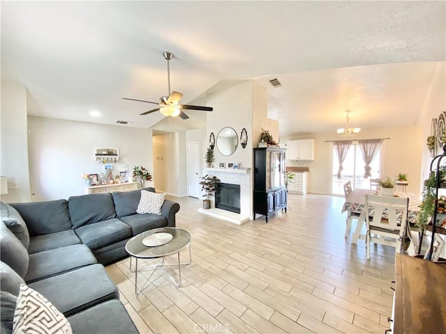 living area featuring light wood finished floors, visible vents, lofted ceiling, and a glass covered fireplace