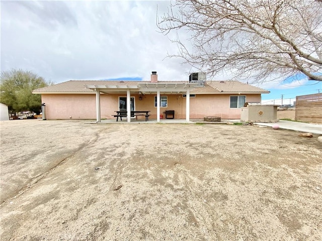 back of house with stucco siding, cooling unit, a chimney, and a patio area