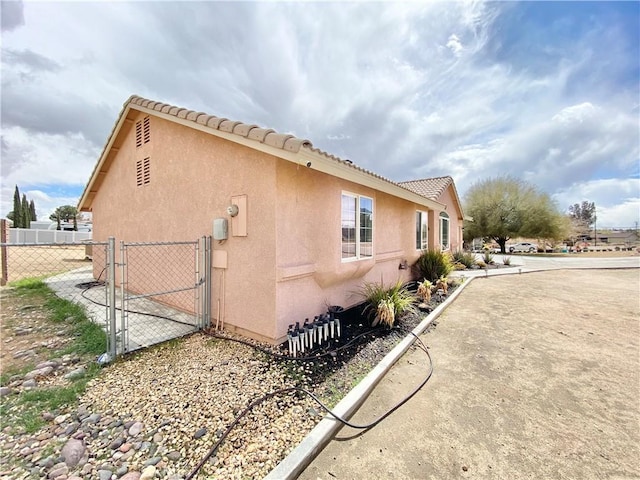 view of side of property featuring a tile roof, a gate, fence, and stucco siding