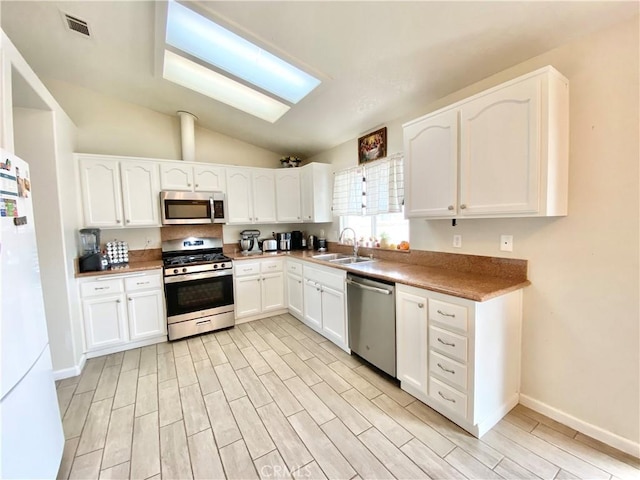 kitchen with wood finish floors, lofted ceiling, appliances with stainless steel finishes, white cabinetry, and a sink