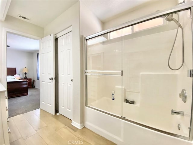 bathroom with ensuite bath, wood finished floors, visible vents, and bath / shower combo with glass door