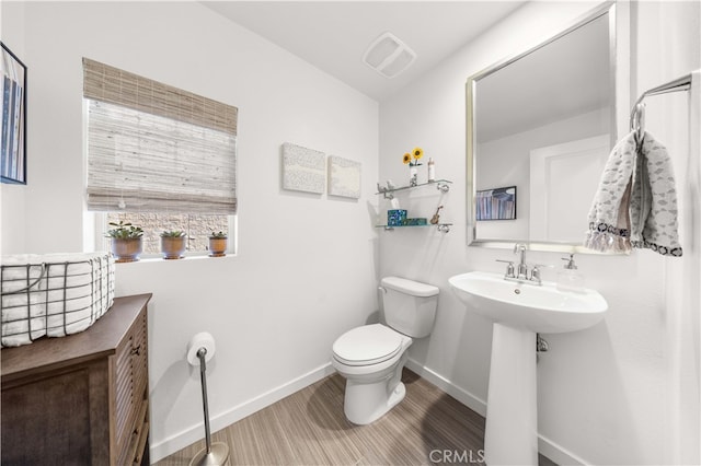 half bath featuring a sink, visible vents, baseboards, and toilet