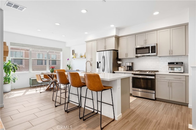 kitchen featuring gray cabinetry, light countertops, decorative backsplash, a kitchen breakfast bar, and stainless steel appliances