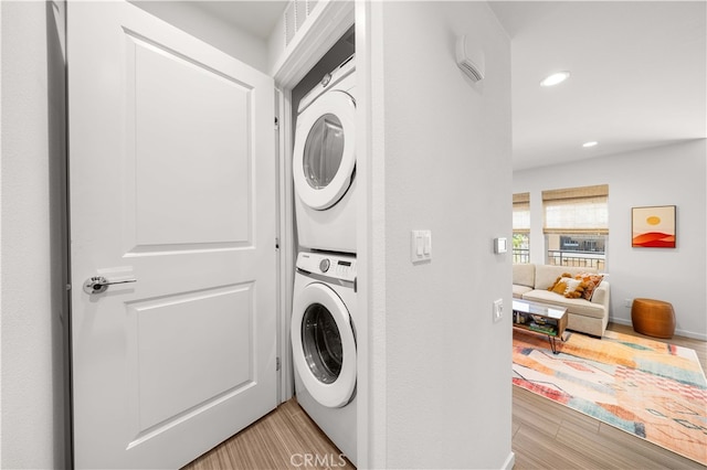 laundry area with stacked washer and dryer, recessed lighting, light wood-type flooring, and baseboards