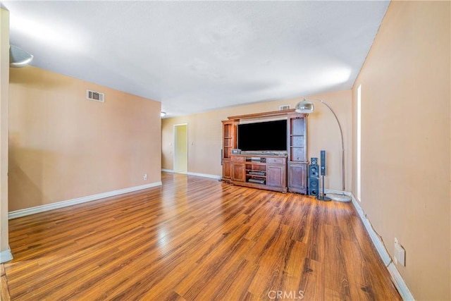 unfurnished living room featuring visible vents, wood finished floors, and baseboards