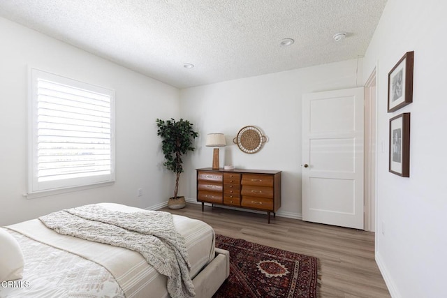 bedroom with baseboards, a textured ceiling, and wood finished floors