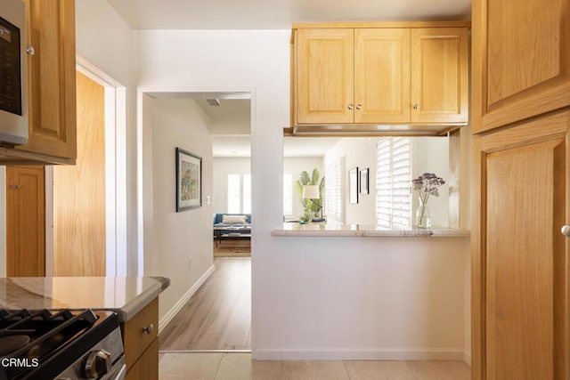 kitchen featuring light tile patterned floors, stainless steel microwave, baseboards, and light brown cabinets