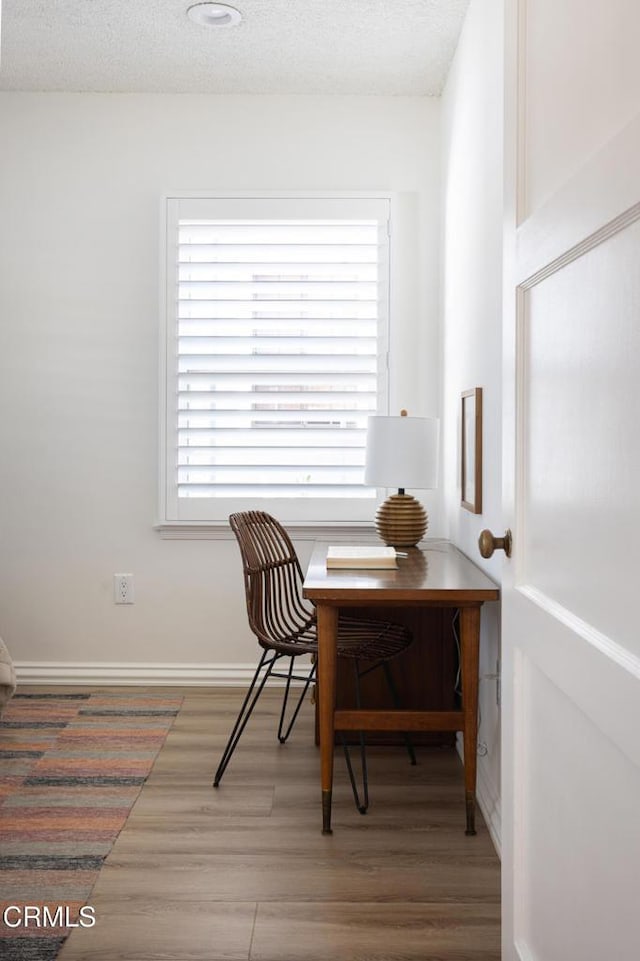 dining space with a textured ceiling, baseboards, and wood finished floors