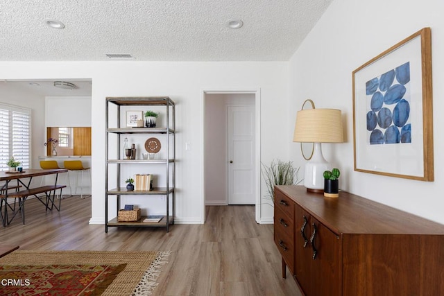 corridor featuring light wood finished floors, visible vents, a textured ceiling, and baseboards