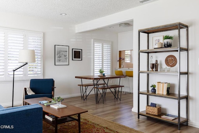 living room featuring visible vents, a textured ceiling, baseboards, and wood finished floors