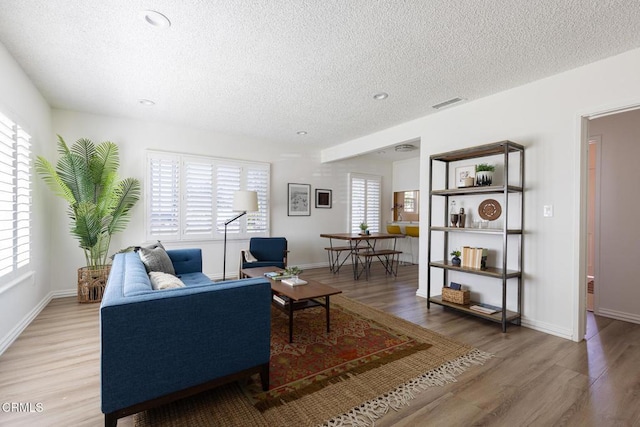 living room featuring light wood finished floors, visible vents, a textured ceiling, and baseboards