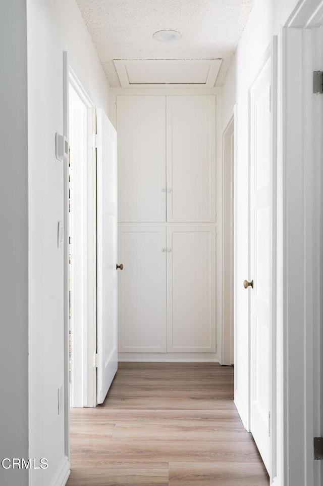 hallway with light wood finished floors and a textured ceiling