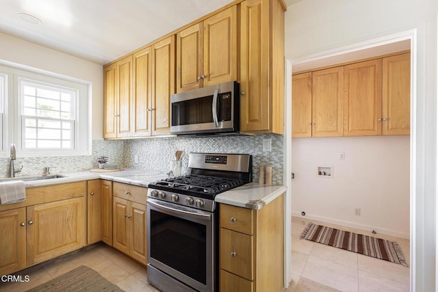 kitchen with light tile patterned flooring, a sink, stainless steel appliances, light countertops, and backsplash