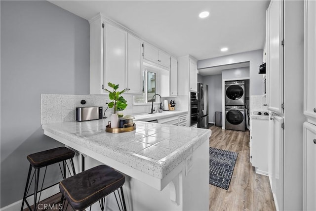 kitchen featuring a peninsula, a sink, decorative backsplash, white cabinets, and stacked washer and clothes dryer