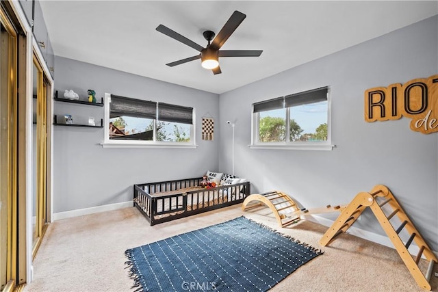 carpeted bedroom with a crib, a ceiling fan, and baseboards