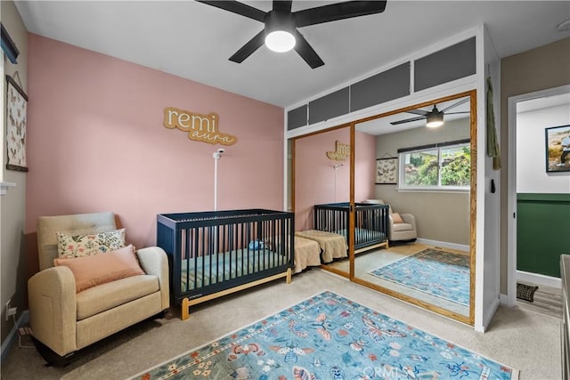 bedroom featuring a closet, a nursery area, carpet flooring, baseboards, and ceiling fan