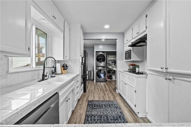 kitchen featuring stacked washing maching and dryer, built in microwave, a sink, white cabinets, and black electric cooktop