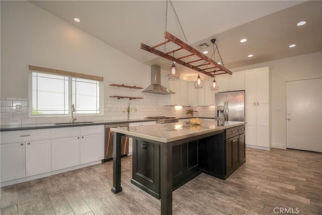 kitchen with tasteful backsplash, light wood-style floors, stainless steel appliances, wall chimney exhaust hood, and a sink