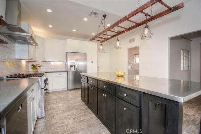 kitchen featuring white cabinetry, decorative backsplash, wall chimney range hood, and appliances with stainless steel finishes