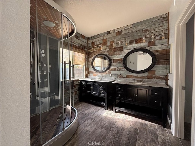 bathroom with double vanity, a shower stall, wood finished floors, and a sink