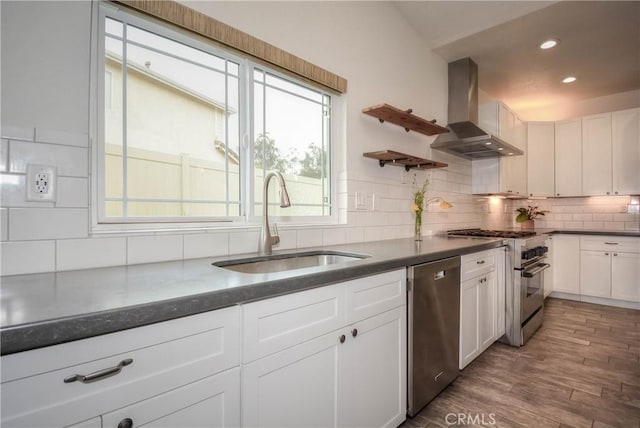 kitchen featuring dark countertops, stainless steel appliances, white cabinetry, wall chimney exhaust hood, and a sink