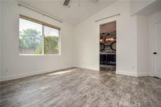 empty room with baseboards, lofted ceiling, wood finished floors, and a ceiling fan