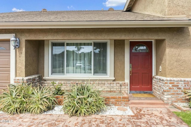 doorway to property featuring brick siding, stucco siding, and a shingled roof