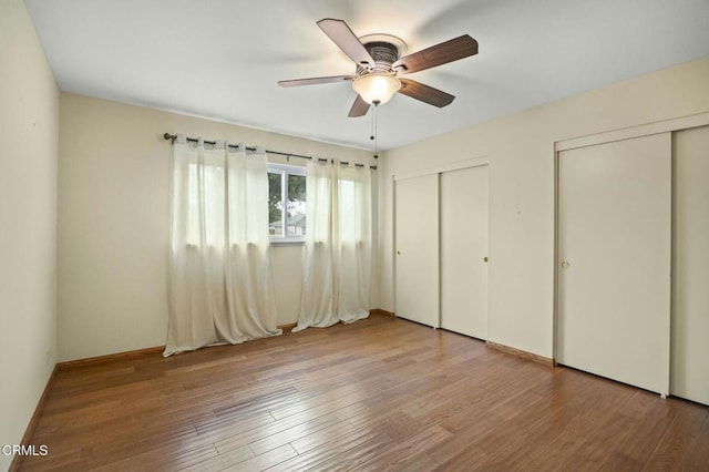 unfurnished bedroom featuring two closets, wood finished floors, and a ceiling fan