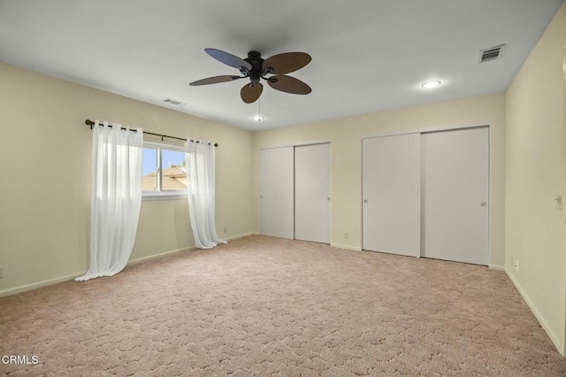 unfurnished bedroom with visible vents, two closets, baseboards, and carpet floors