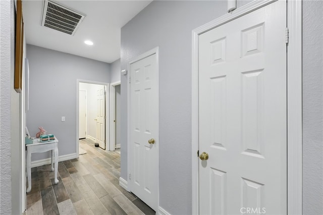 hallway with recessed lighting, wood finished floors, visible vents, and baseboards