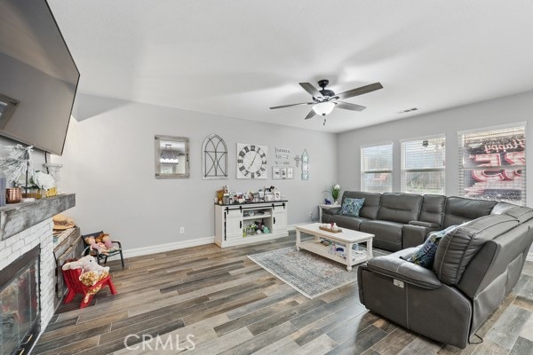 living area featuring a glass covered fireplace, a ceiling fan, baseboards, and wood finished floors