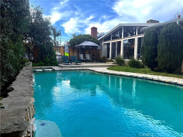 pool featuring a gazebo, glass enclosure, fence, and a patio area