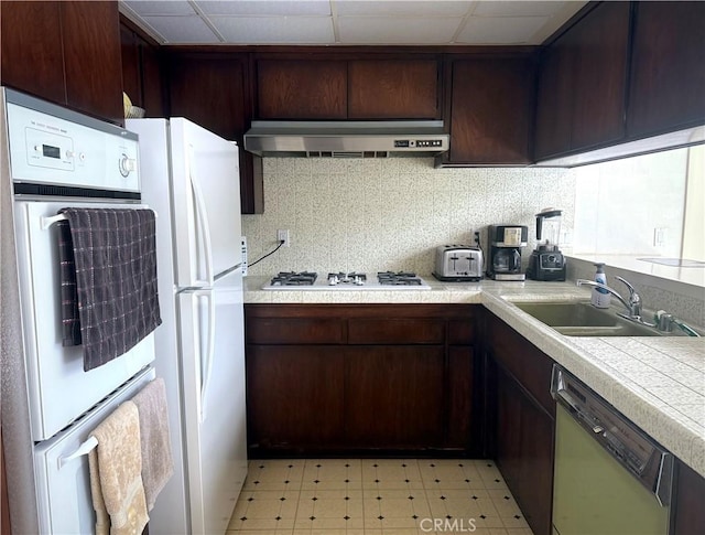 kitchen featuring under cabinet range hood, a sink, white appliances, light countertops, and light floors