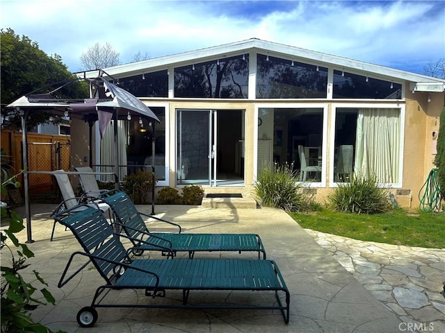 rear view of property featuring stucco siding, a sunroom, a patio, and fence