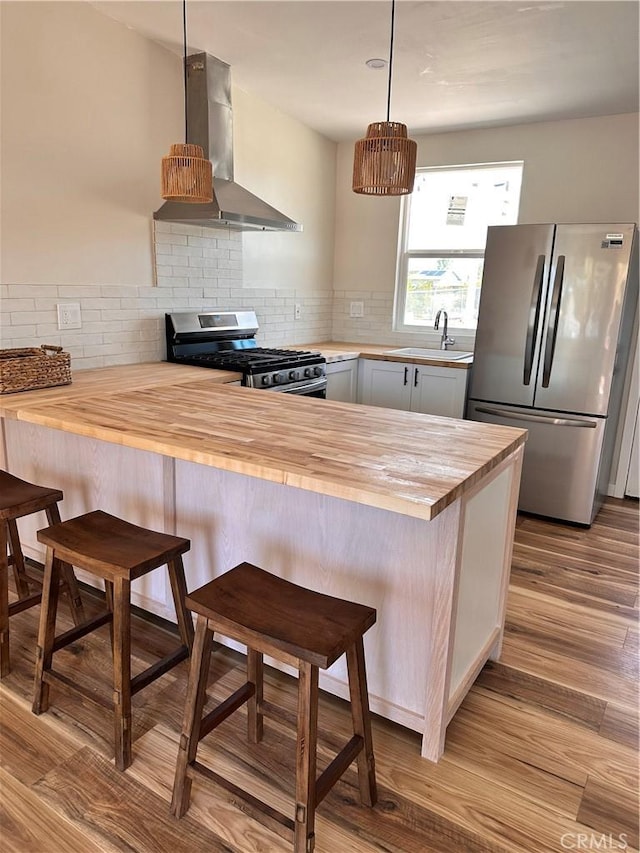 kitchen featuring range hood, wooden counters, a sink, stainless steel appliances, and tasteful backsplash