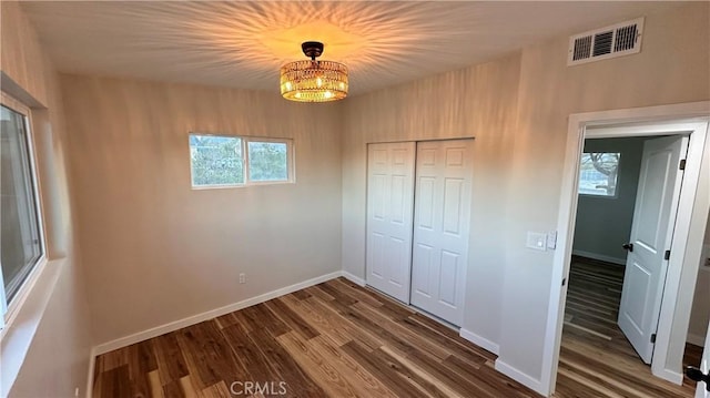 unfurnished bedroom with dark wood-type flooring, baseboards, visible vents, and a closet