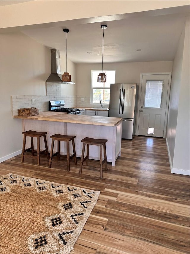 kitchen featuring wall chimney range hood, stainless steel appliances, a peninsula, a breakfast bar area, and light countertops