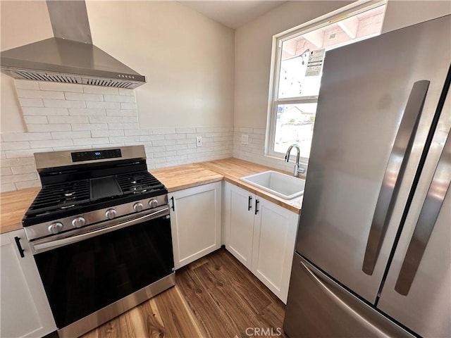 kitchen featuring wall chimney range hood, appliances with stainless steel finishes, dark wood-style floors, wood counters, and a sink