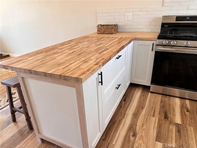 kitchen featuring tasteful backsplash, wood finished floors, gas stove, white cabinetry, and wood counters