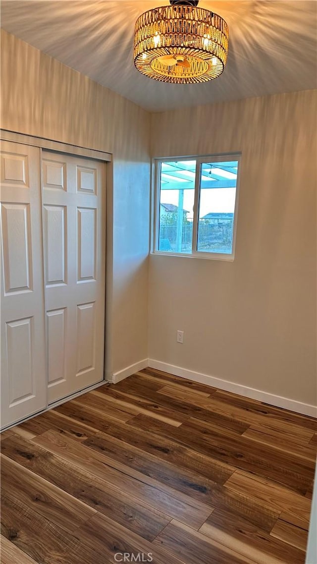 unfurnished bedroom with baseboards, dark wood-style flooring, and a closet